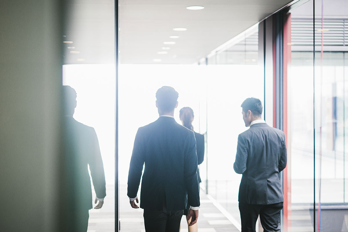 Group of business men and women walking through modern office in the distance with all their backs facing photo