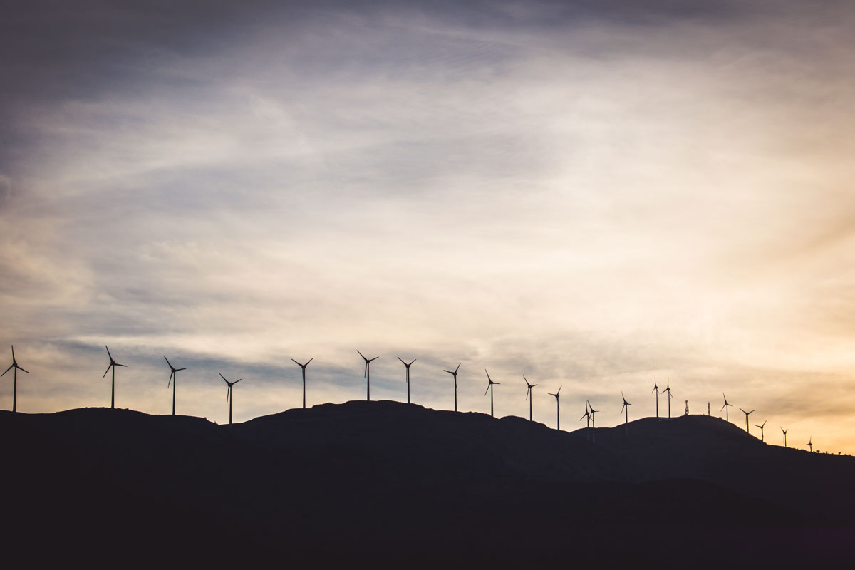 sunset view of a range of energy construction wind turbines lined up on a hill or mountain with an orange sky in the background