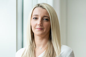 head shot of Augusta Business women dressed in formal shirt and personal assistant to managing directors, Lucy Kirby, smiling and posing for photo in bright modern London office room next to wide and floor to ceiling windows