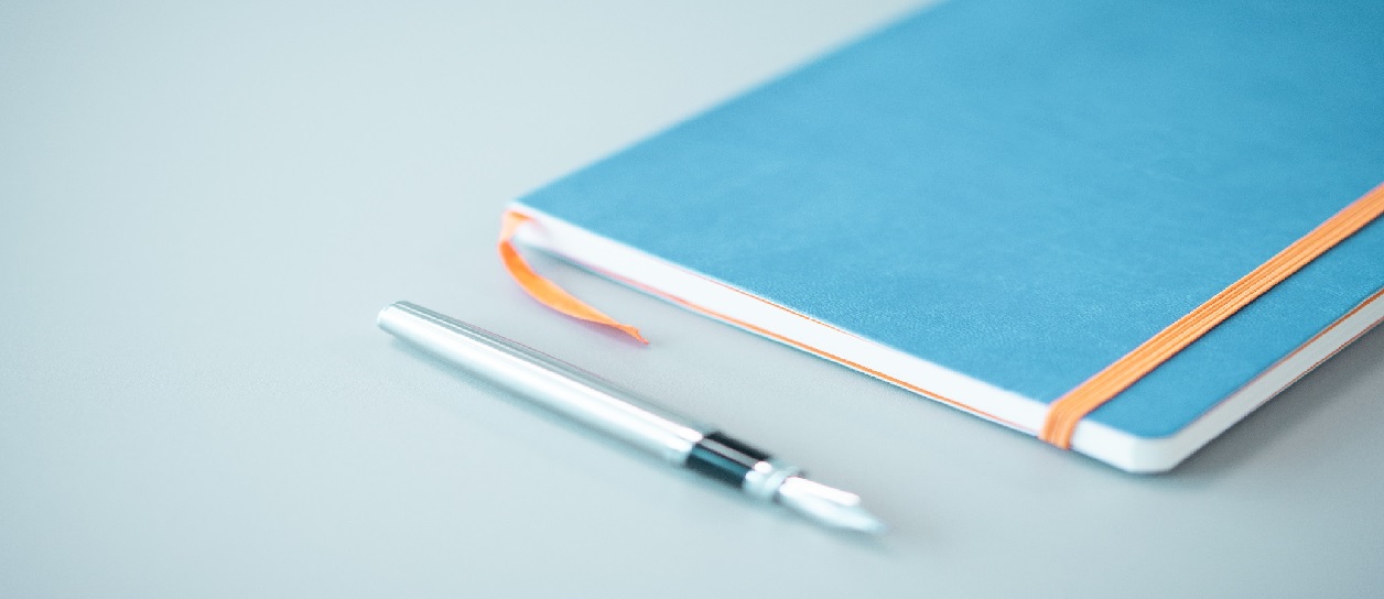 Blue notepad with orange placeholder tape on a grey office table during the day with silver fountain table next to it