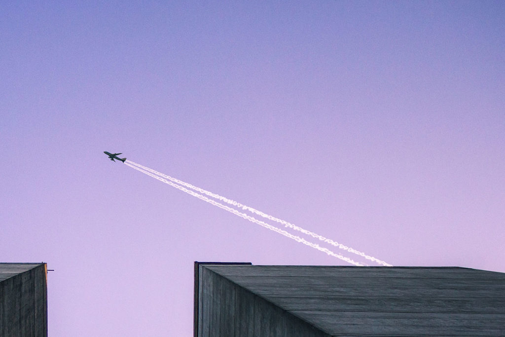 ground to sky view of international flight plane flying over skyscraper buildings with a purple sky