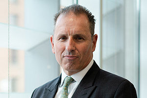 head shot of Augusta Business man dressed in suit managing director and founding partner Robert Hanna standing and posing for photo in bright modern London office room next to wide and floor to ceiling windows