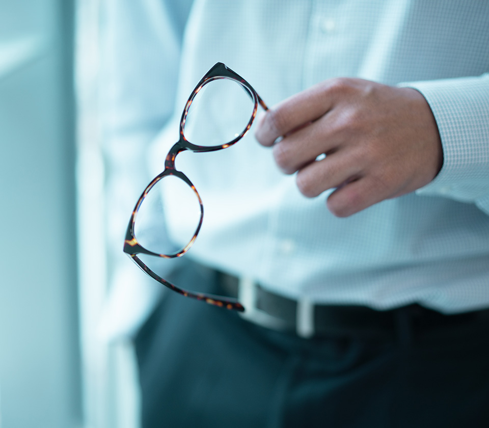 business man standing and holding formal work glasses with other hand in pocket with only half his torso showing