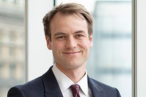 Head Shot of Augusta Business man dressed in suit Investment manager in the diligence team Andrew Roberts standing and posing for photo in bright modern London office room next to wide and floor to ceiling windows