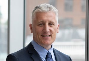 Augusta Business man dressed in suit country manager of Canada Max Doyle standing and posing for photo in bright modern London office room next to wide and floor to ceiling windows