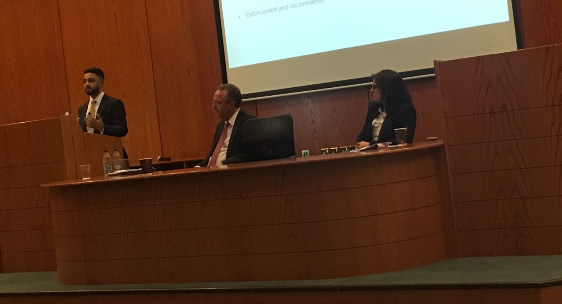 Mohsin Patel, business man and lawyer, head of originations at Augusta litigation funder, presenting behind a podium on a panel with two other people to a room of lawyers