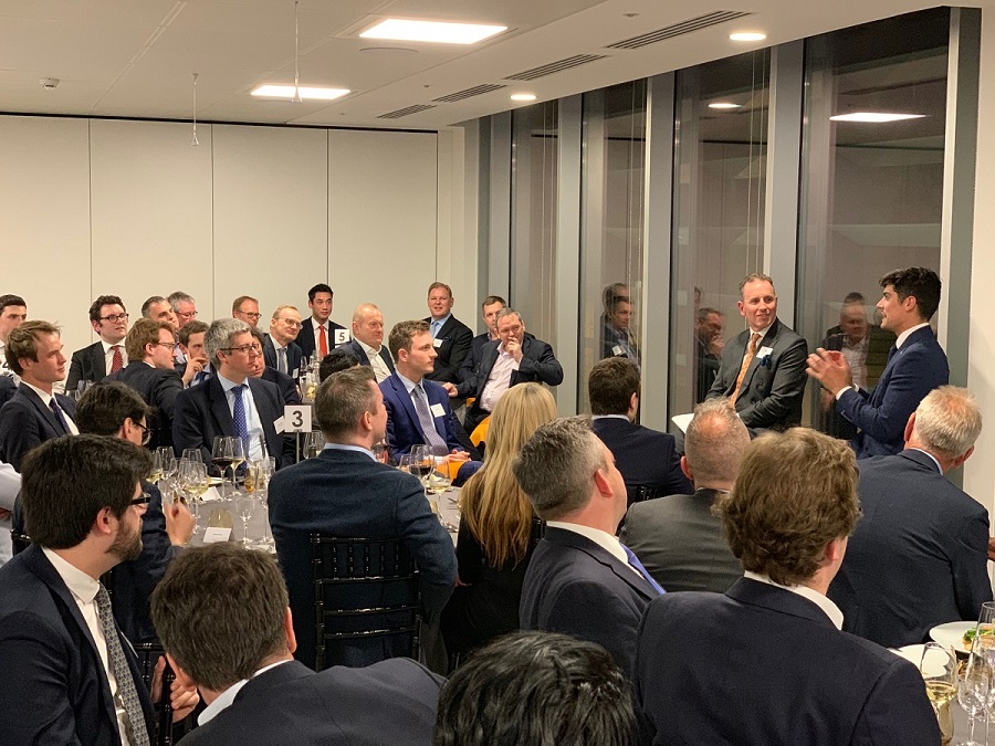 Modern Augusta Litigation Funder boardroom filled with 50 people sitting around round tables while listening to former England Cricket captain Alistair Cook speaking during a night time event