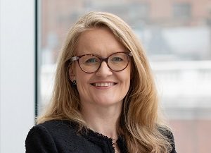 Head shot of Augusta Business women dressed in formal dress Chief Operating Officer COO Polly Bahl standing and posing for photo with a smile in bright modern London office room next to wide and floor to ceiling windows