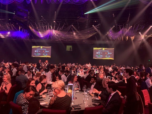 Large crowd of seated business people in a large hall at an awards event. Speaking at round tables