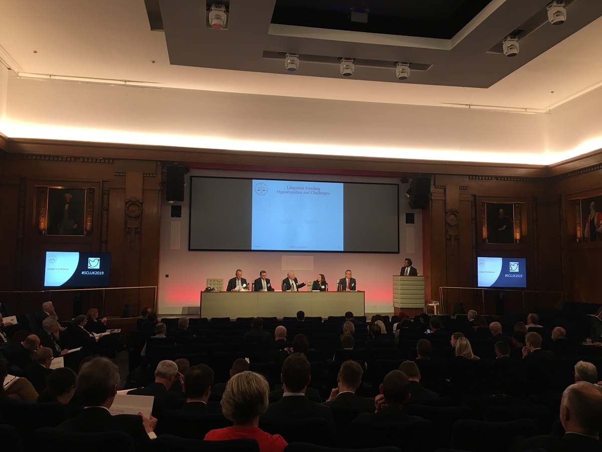 Large room and auditorium filled with business people facing a panel of litigation funders presenting during an event